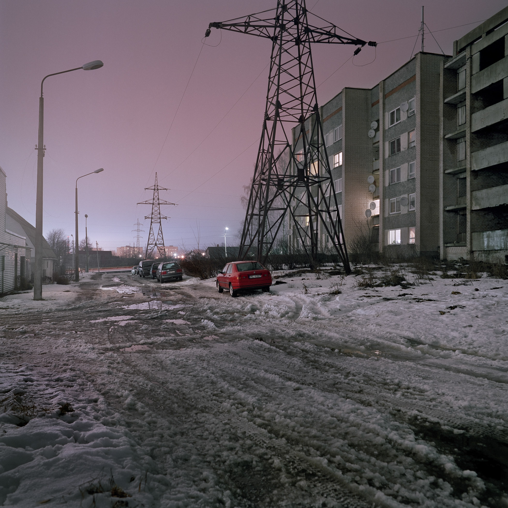 A red car is parked on the side of a snowy road.