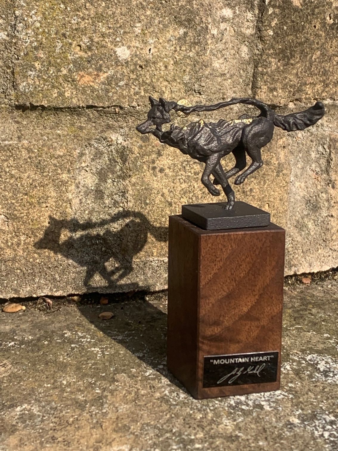 A bronze statue of a running horse on a wooden base.