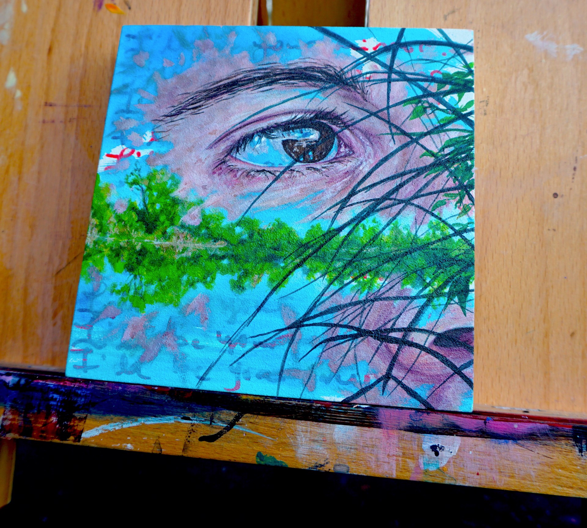 A close-up of a person's eye partially obscured by dark grass, with a landscape reflected in the iris.