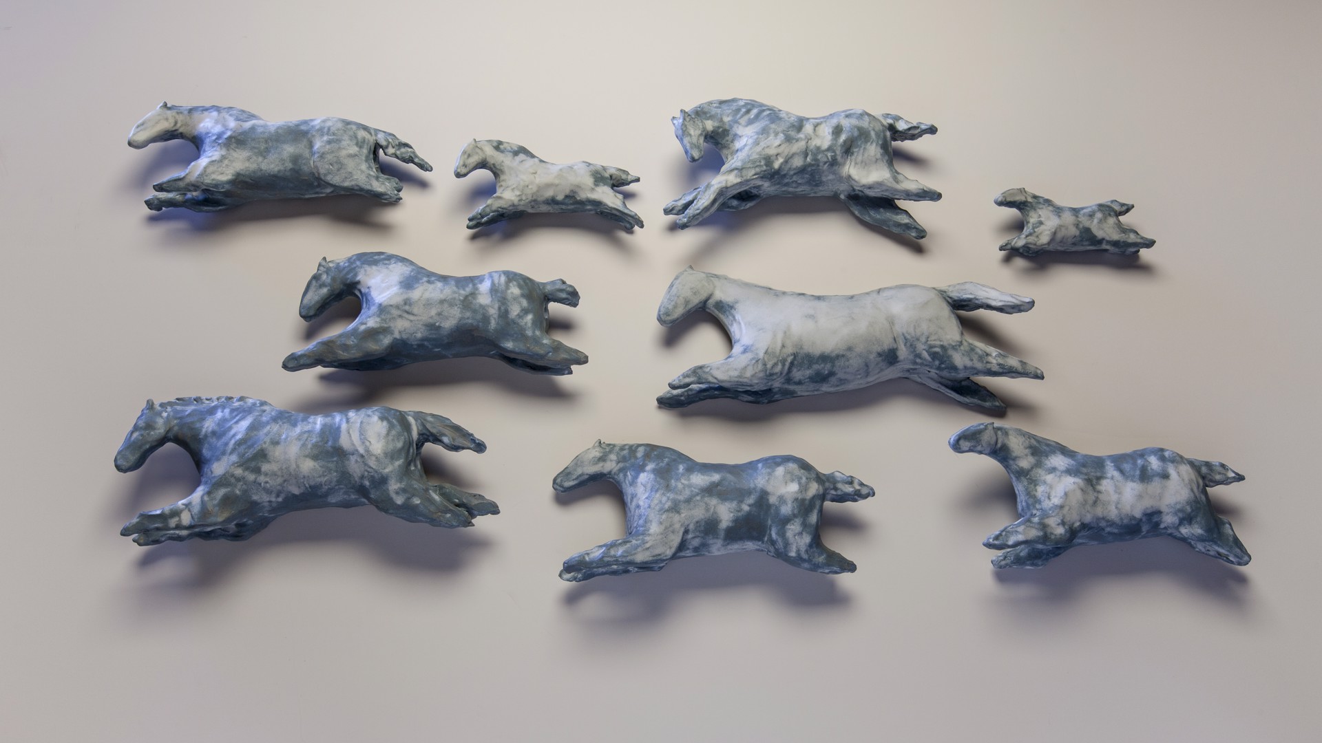 A group of blue and white horses running on a white surface.