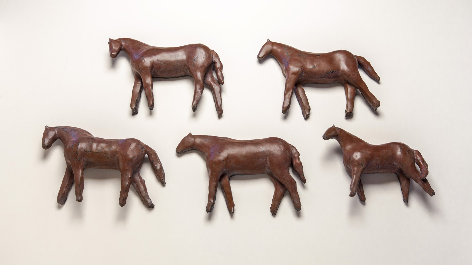 A group of four bronze horses on a white surface.