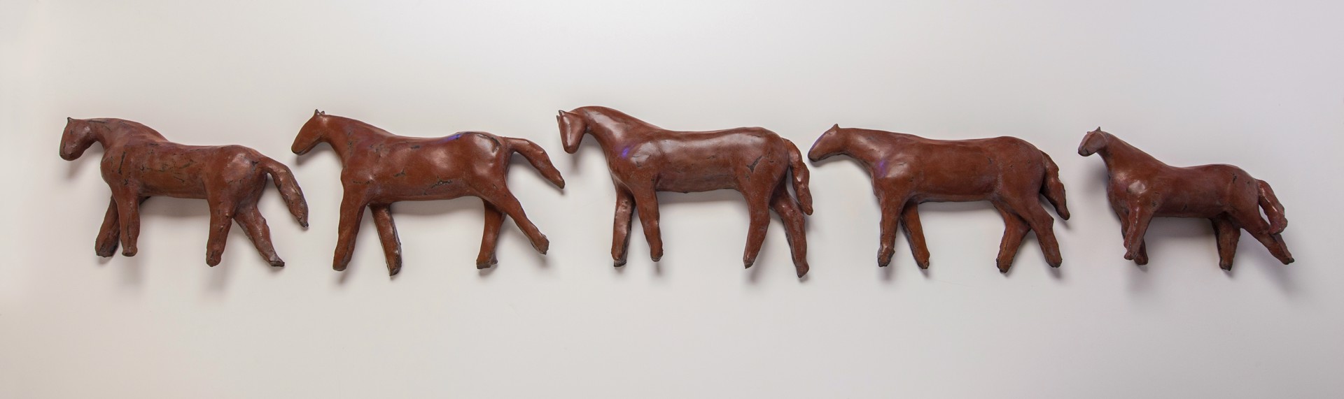 A group of four bronze horses on a white surface.