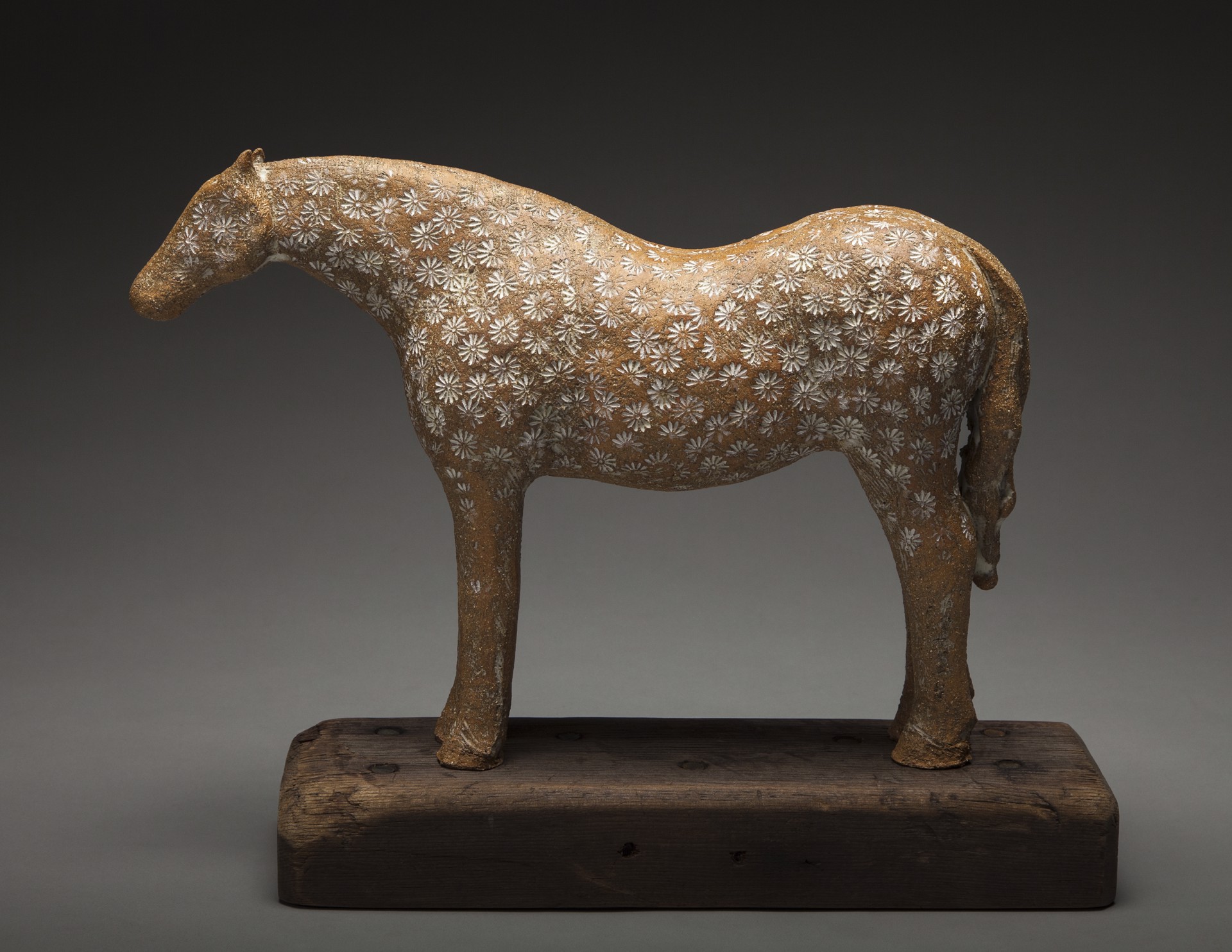 A ceramic horse sculpture with a floral pattern standing on a wooden base.