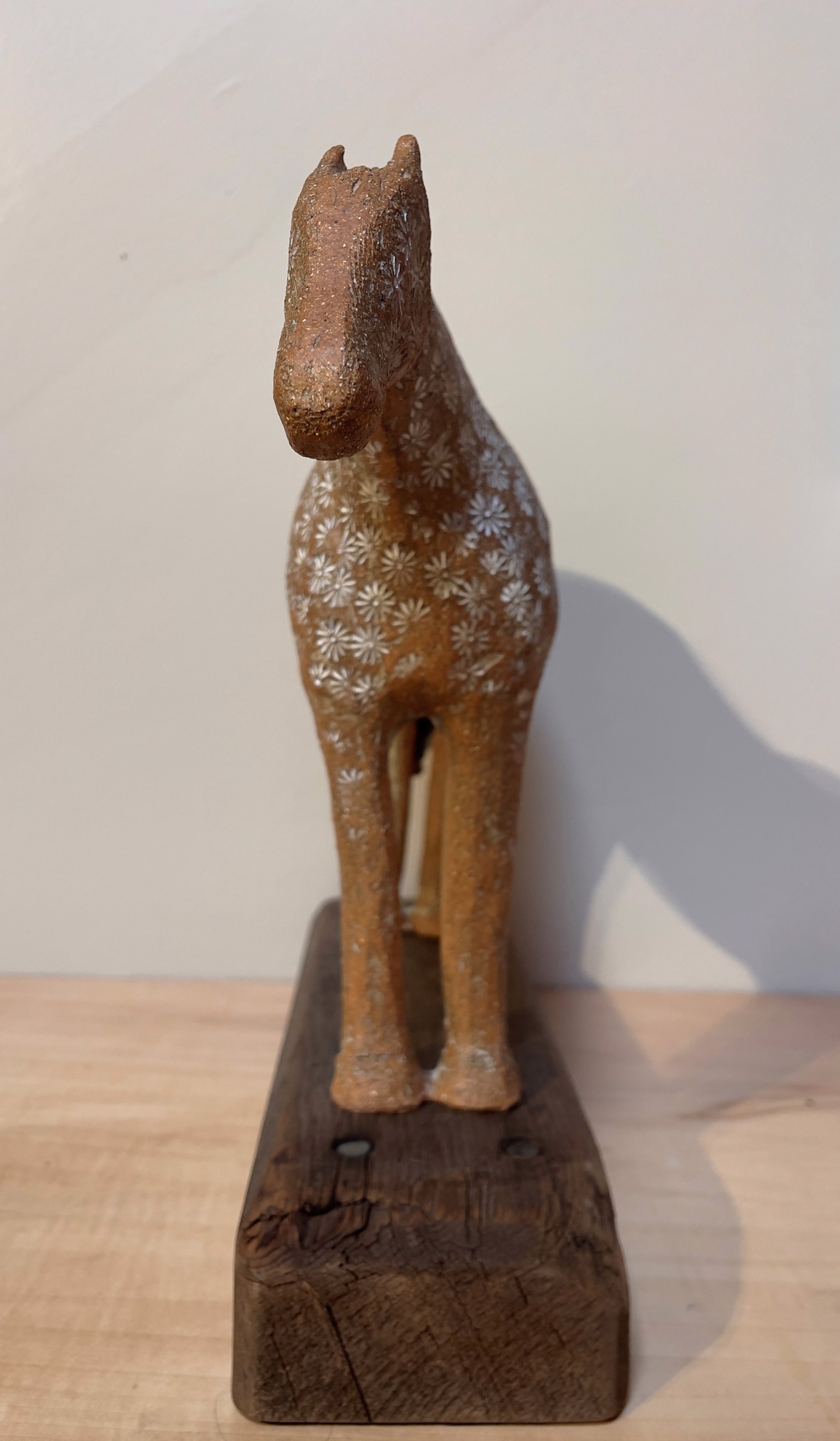 A ceramic horse sculpture with a floral pattern standing on a wooden base.