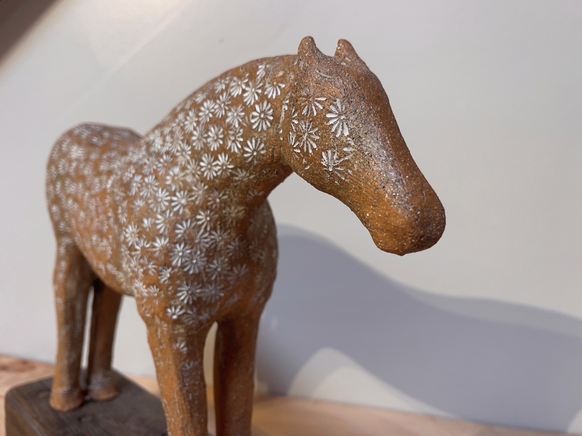 A ceramic horse sculpture with a floral pattern standing on a wooden base.