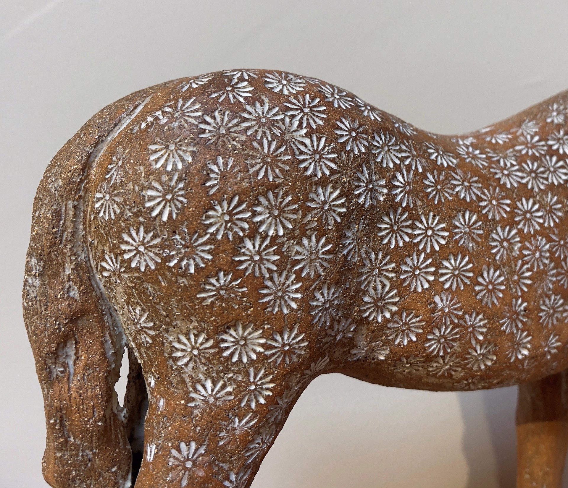 A ceramic horse sculpture with a floral pattern standing on a wooden base.