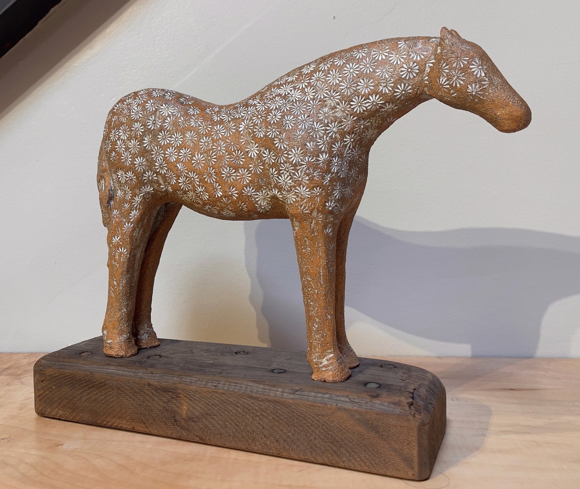 A ceramic horse sculpture with a floral pattern standing on a wooden base.