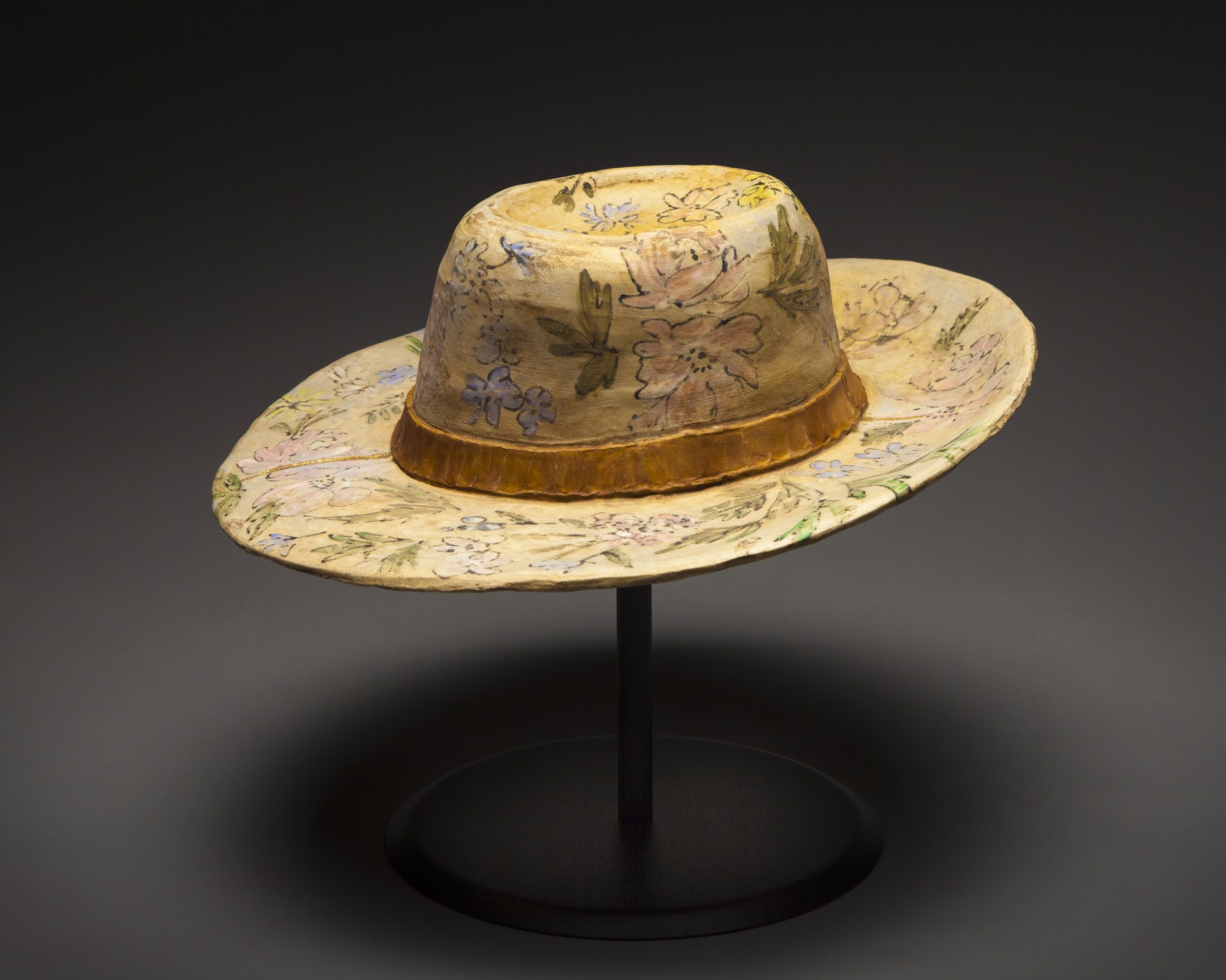 A floral-patterned hat displayed on a black stand against a dark background.