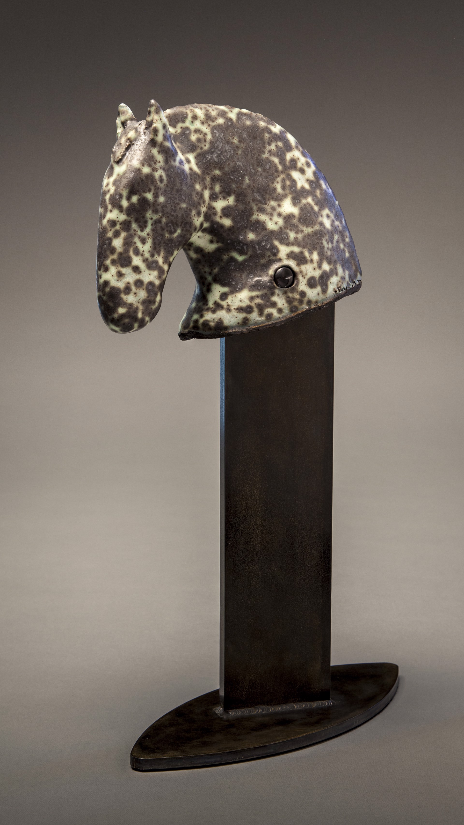 A sculptural horse head mounted on a dark wooden stand.
