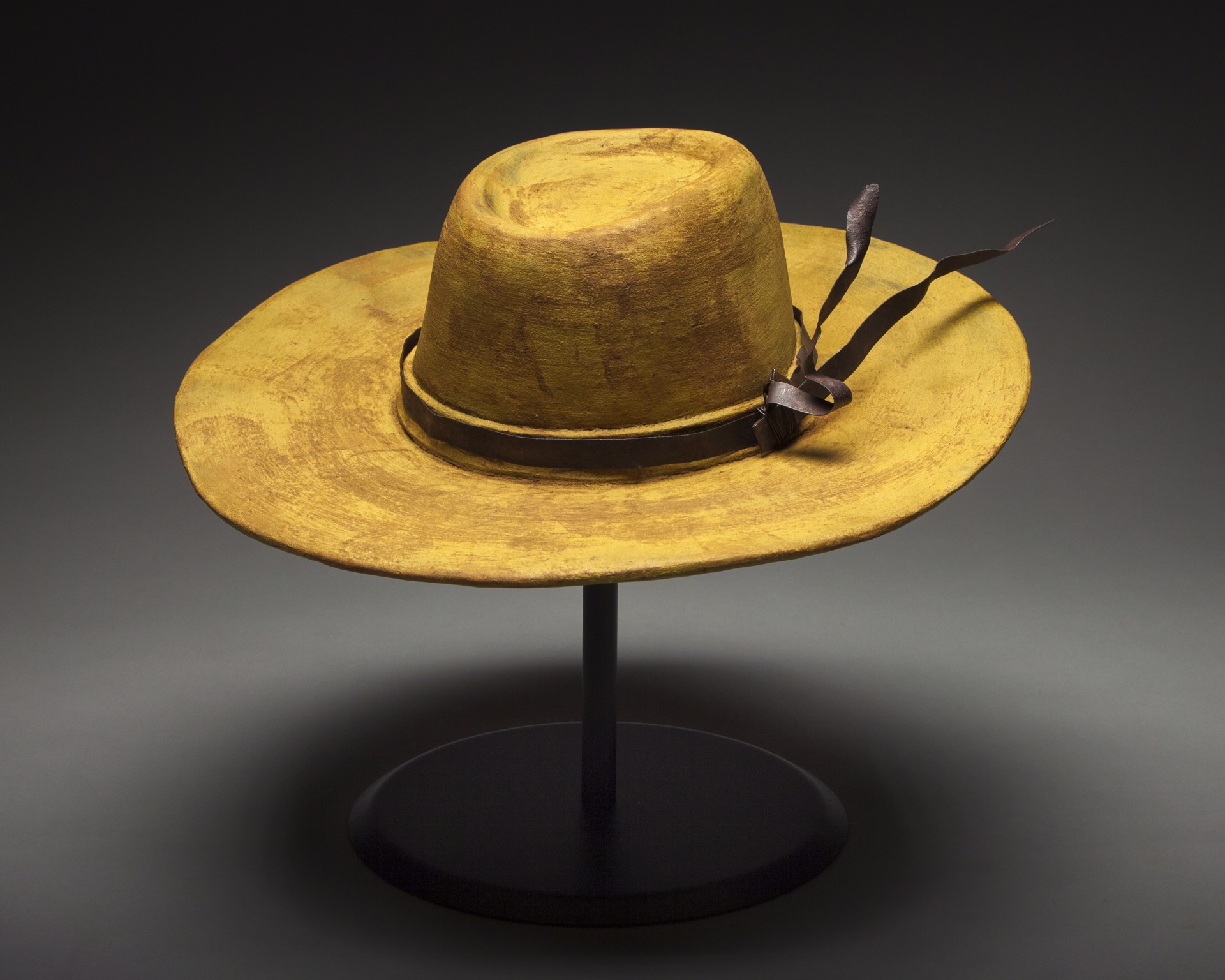 A yellow hat on a black stand on a gray background.