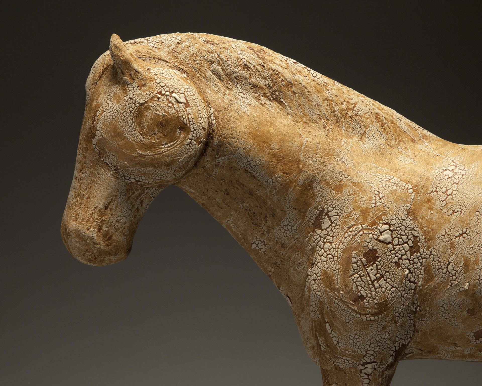 A weathered horse sculpture stands on a dark wooden base against a neutral gradient background.