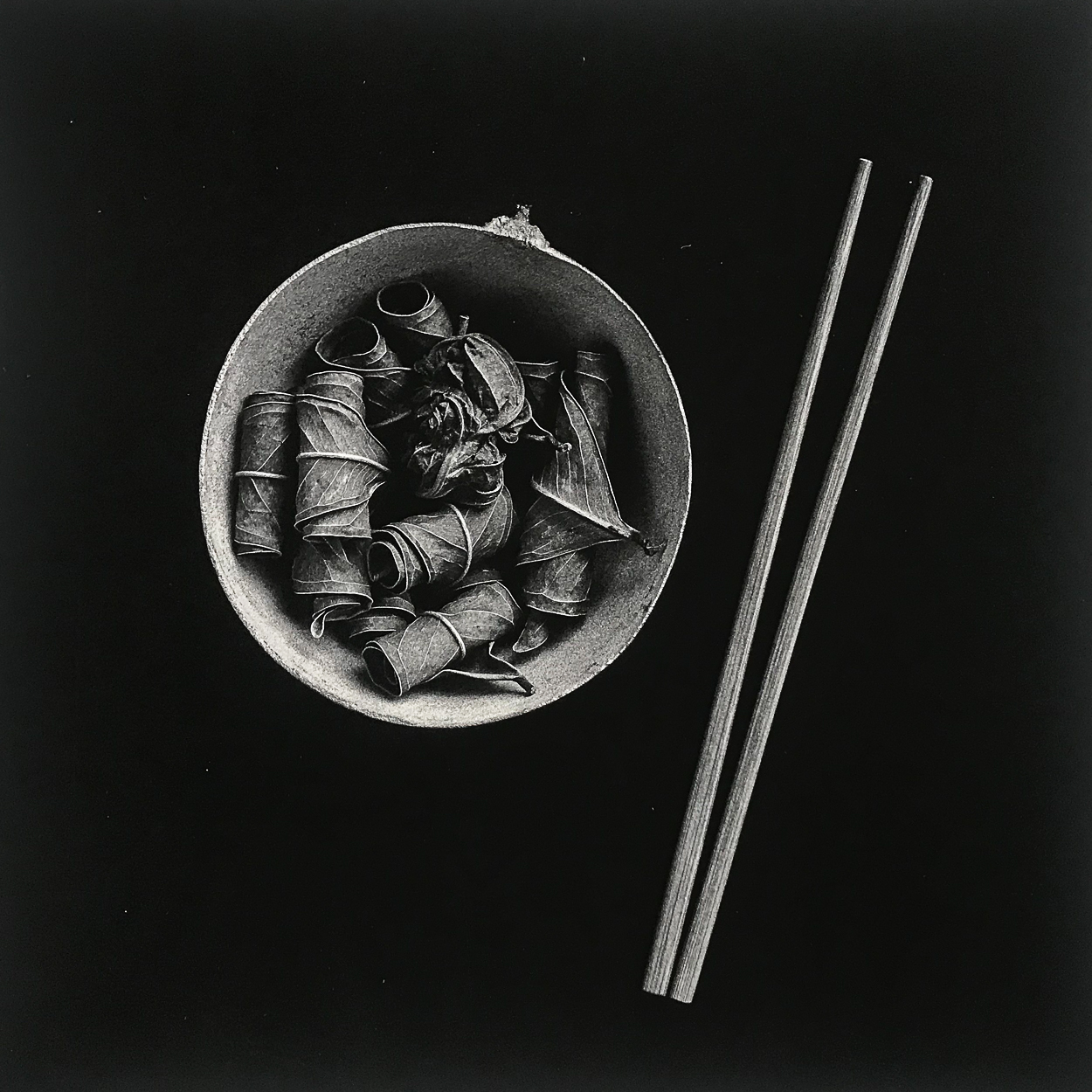 A black and white photo of a bowl of food with chopsticks.