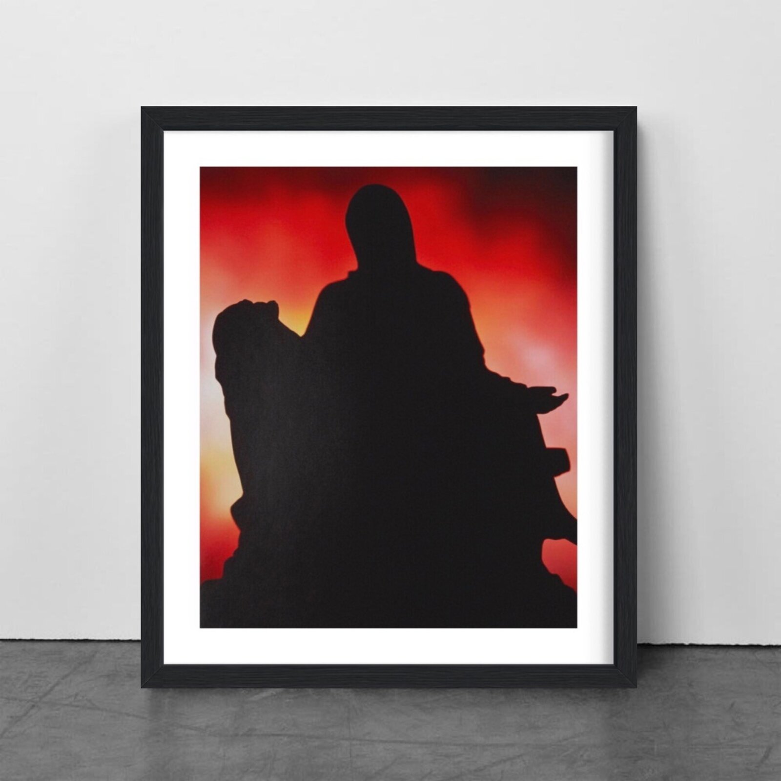 A framed print featuring a black silhouette of a figure against a fiery red and orange background.