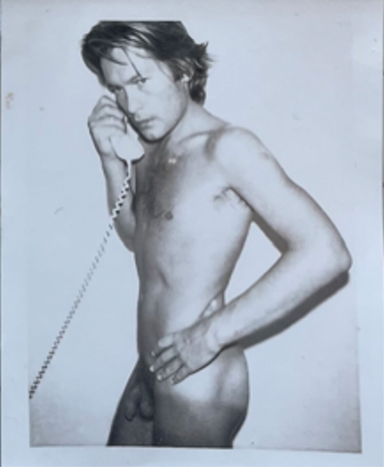 A shirtless man talking on a telephone. 