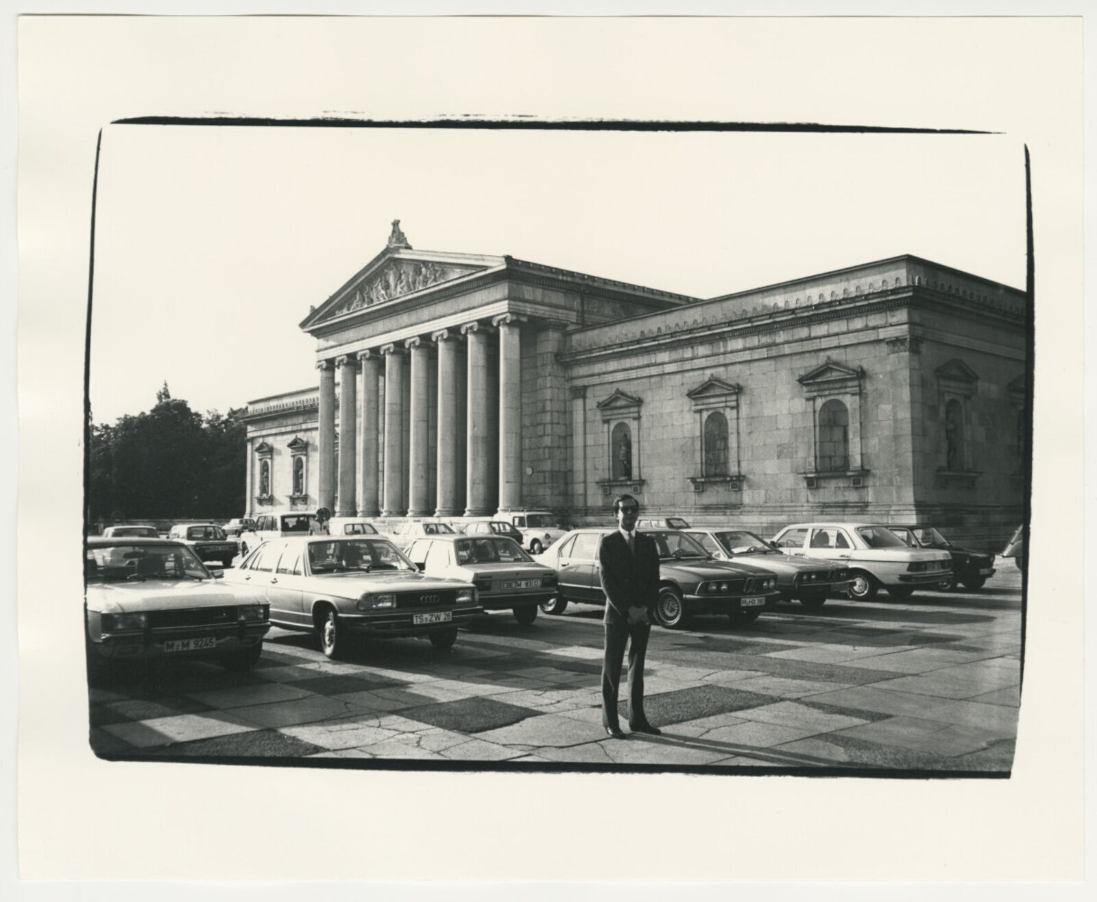 A black and white photo of a man standing in front of a building.