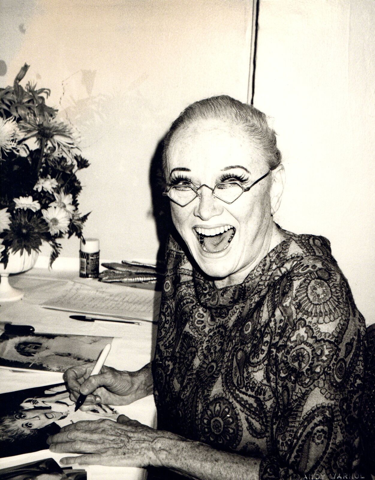 A black and white photo of a woman sitting at a table with a pen.
