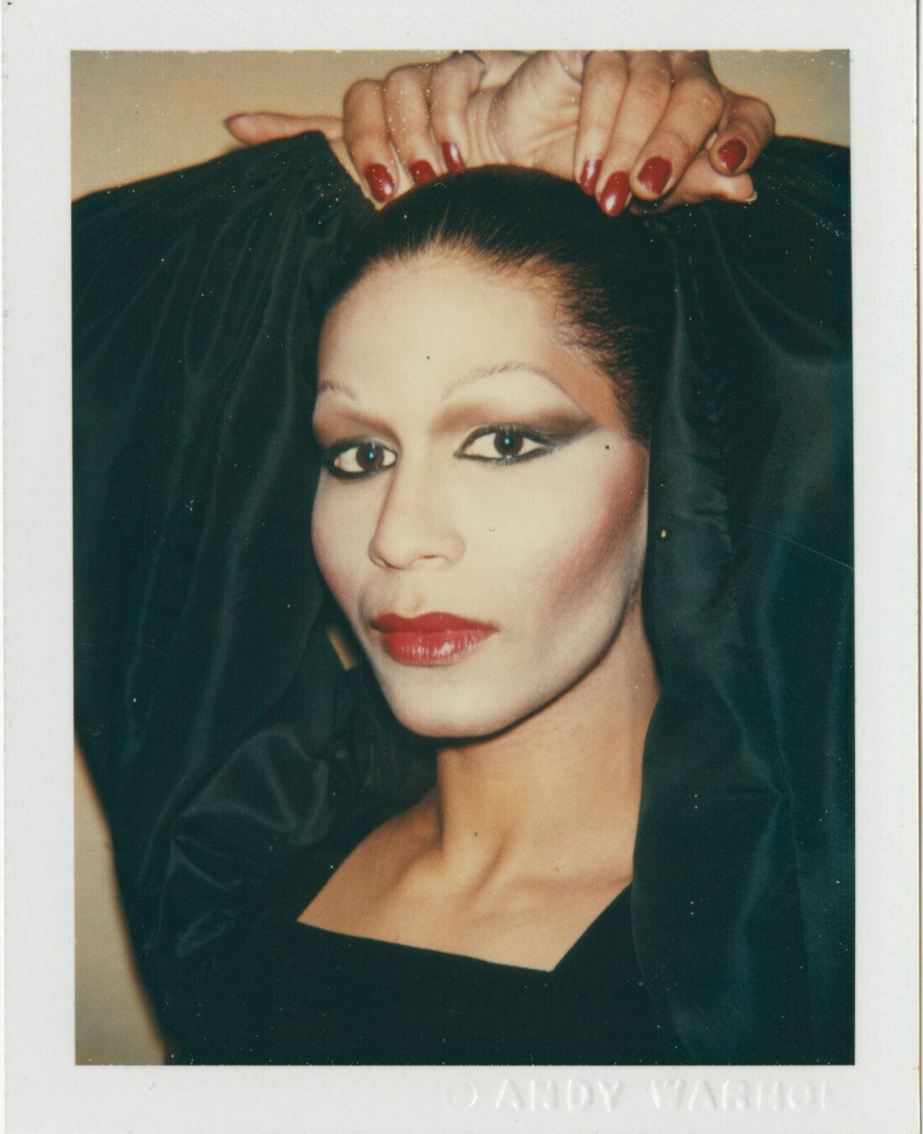 A polaroid photo of a woman with red nails and a black dress.