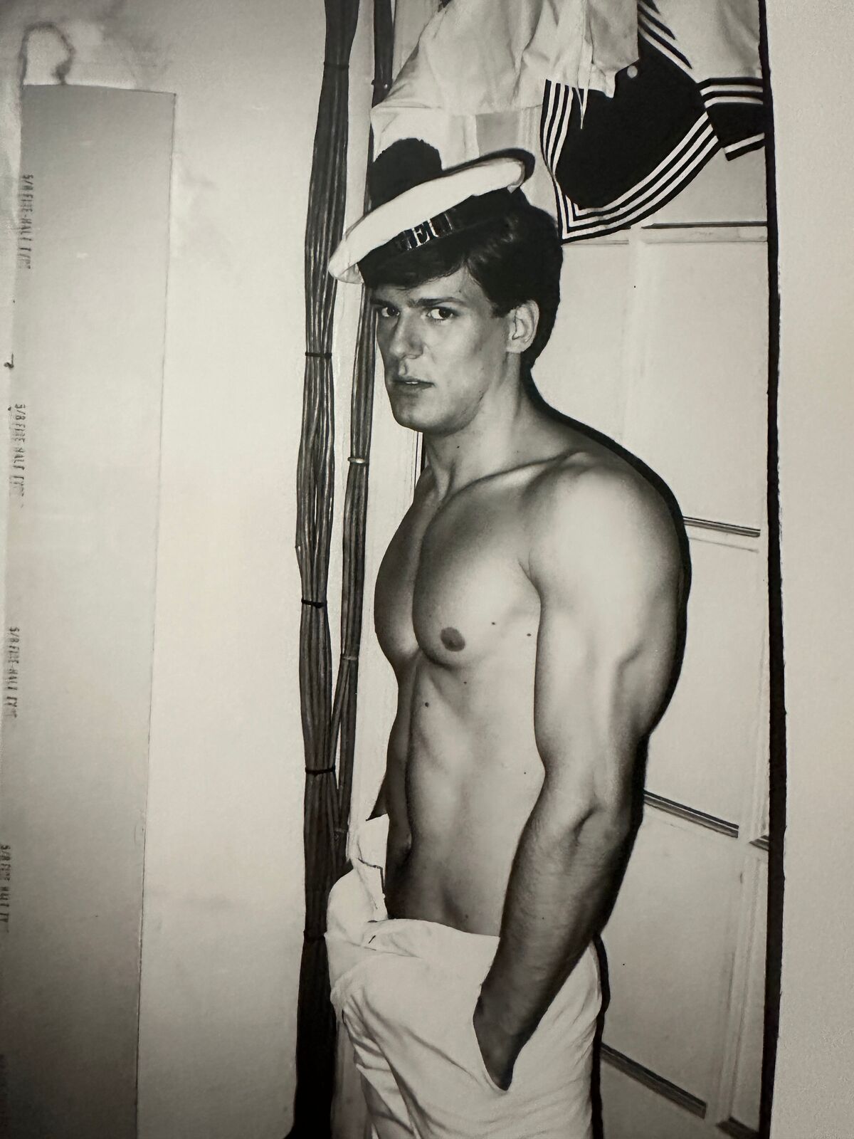 A shirtless man in a sailor's hat standing in front of a door.