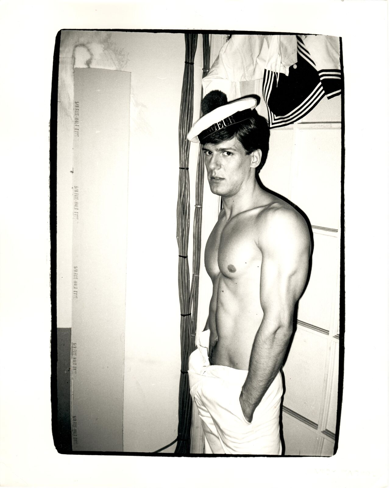 A shirtless man in a sailor's hat standing in front of a door.
