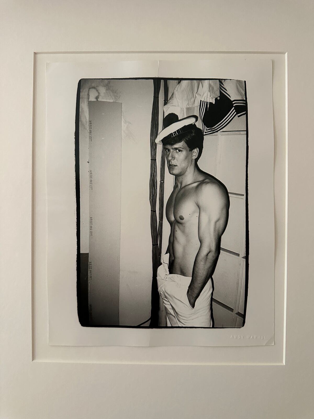 A shirtless man in a sailor's hat standing in front of a door.