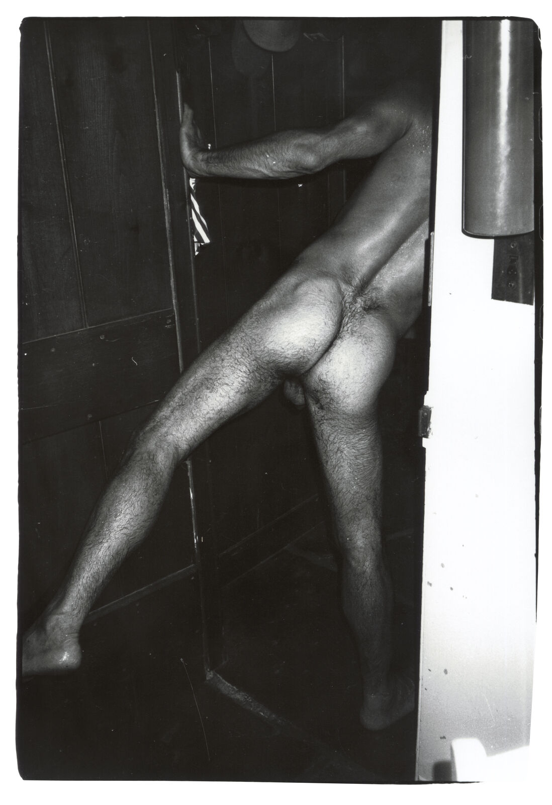A naked man leaning against a door in a bathroom.