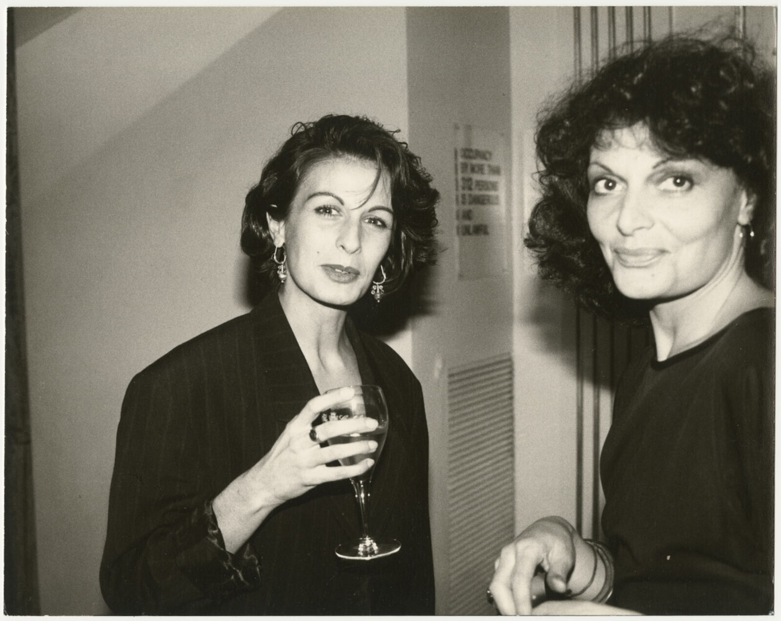 Two women standing next to each other holding wine glasses.