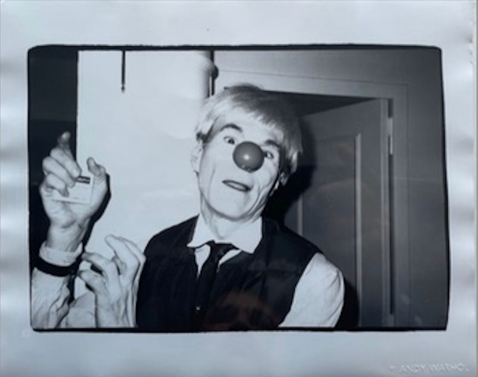 A black and white photo of a clown holding a cigarette.