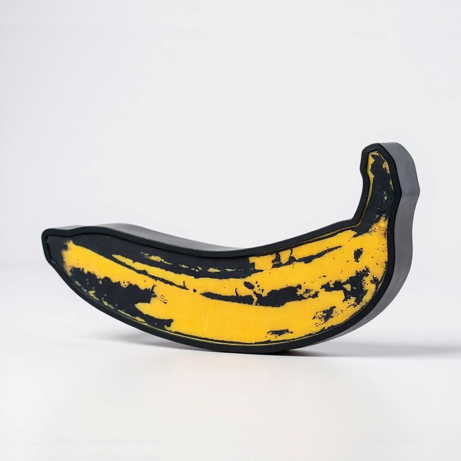 A yellow and black banana shaped object on a white surface.