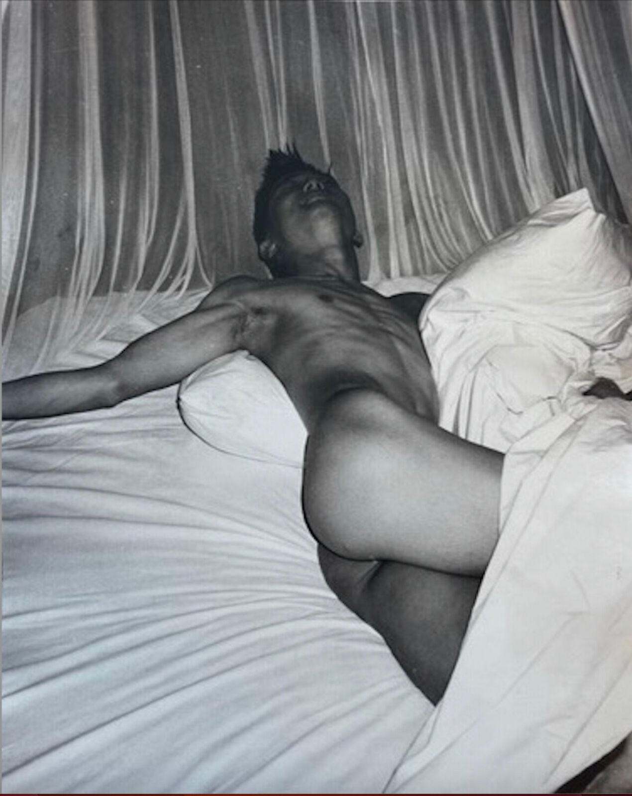 A naked man laying on a bed with white sheets.