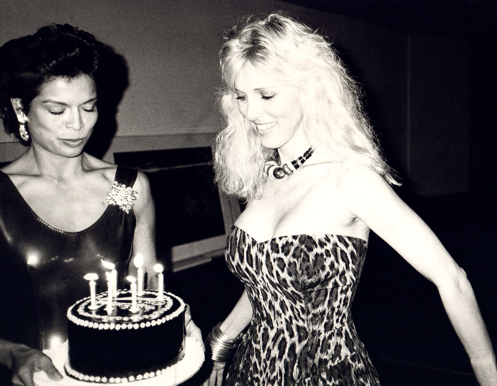 A woman in a leopard print dress holding a birthday cake with lit candles.