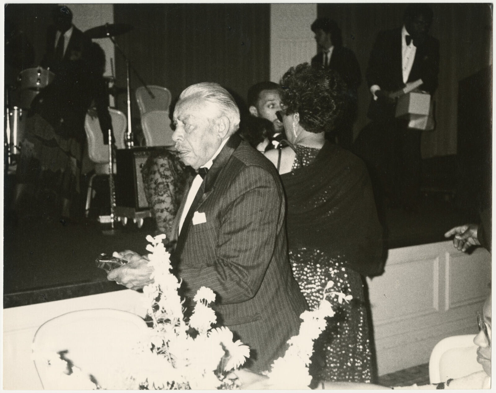 A black and white photo of a man in a tuxedo sitting at a table.