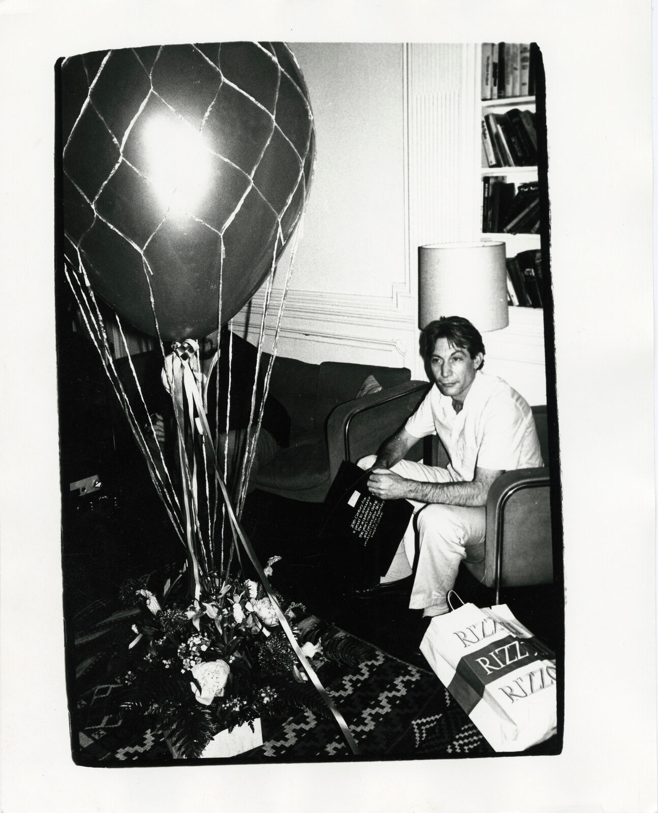 A black and white photo of a man sitting in a chair with a balloon.