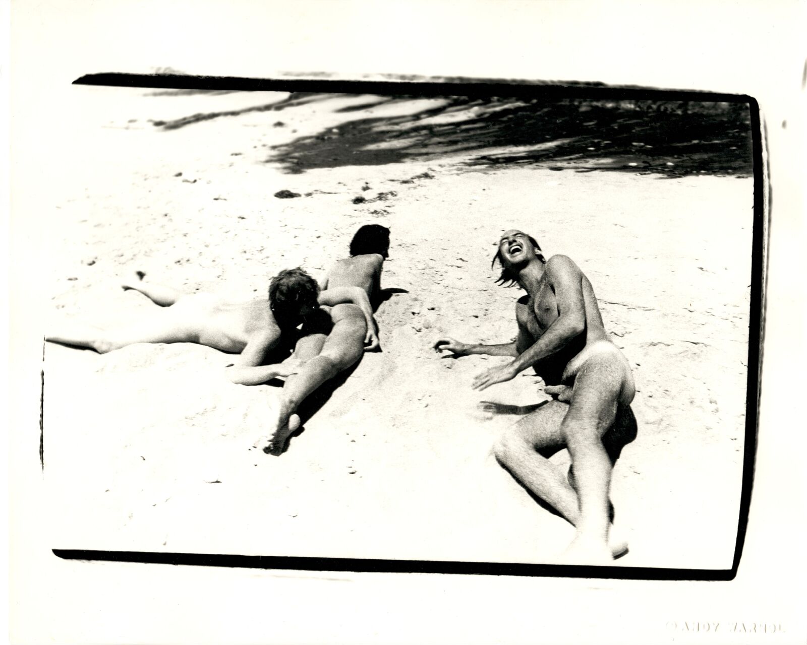 A black and white photo of three naked people on the beach.
