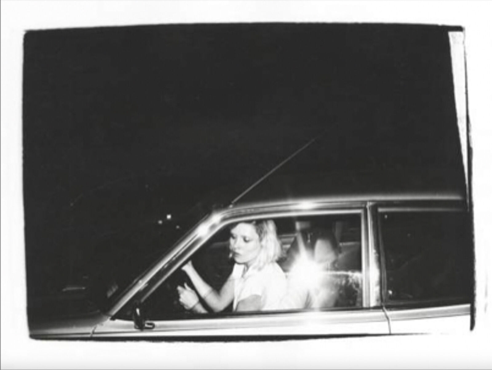 A black and white photo of a woman sitting in a car.