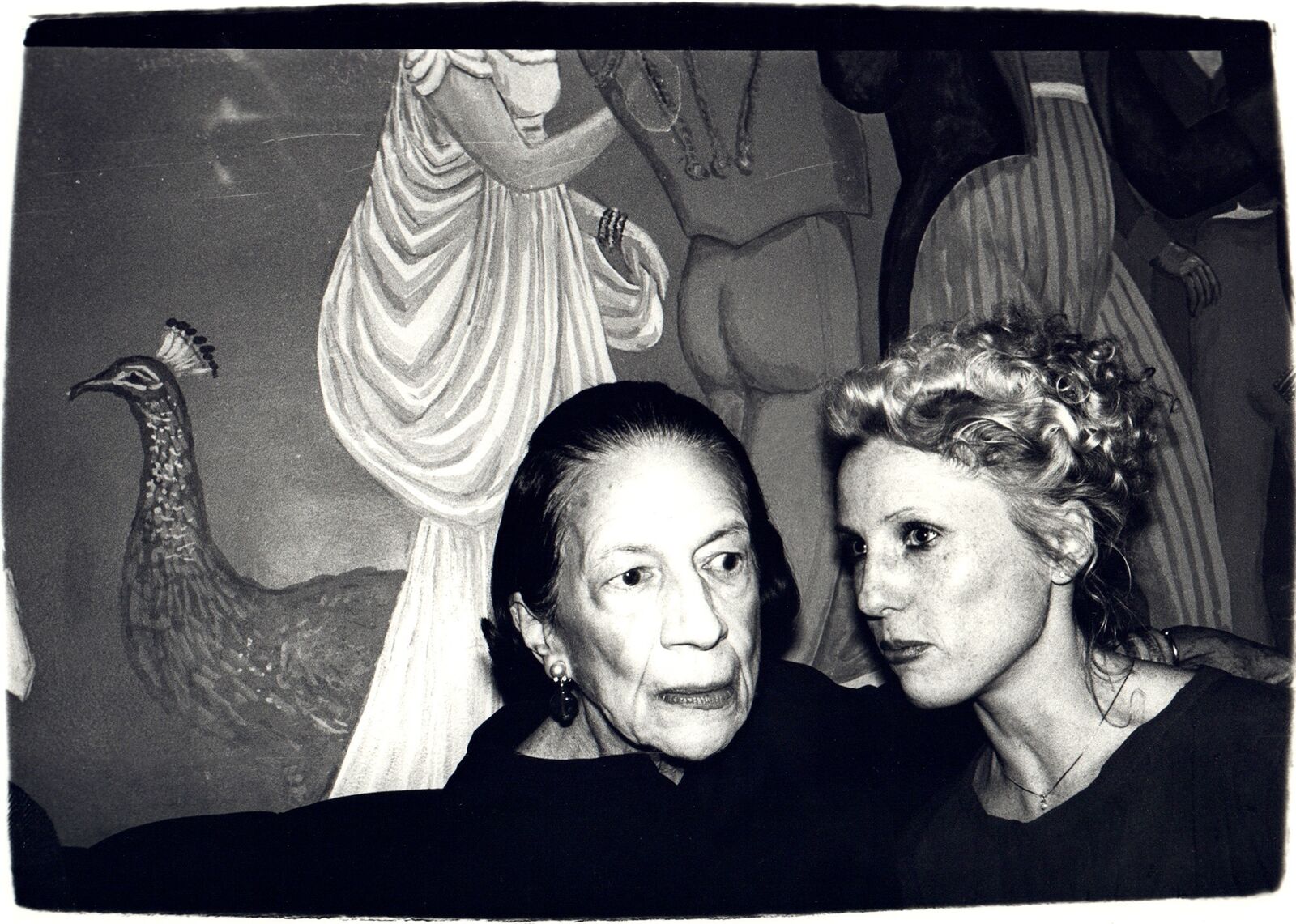 A black and white photo of two women in front of a painting.