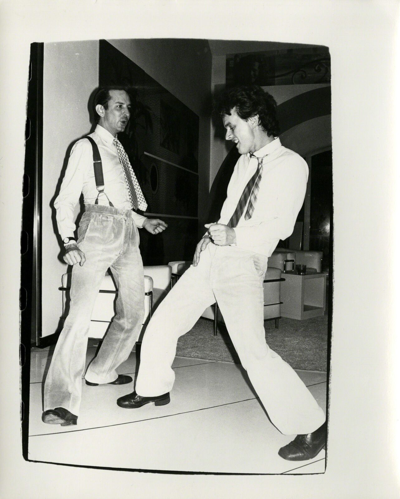A black and white photo of two men dancing in a room.