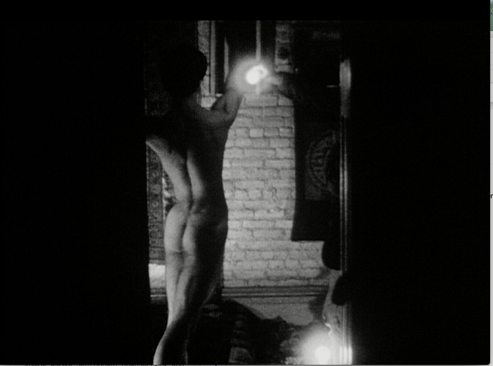 A naked man standing in front of a brick wall holding a flashlight.
