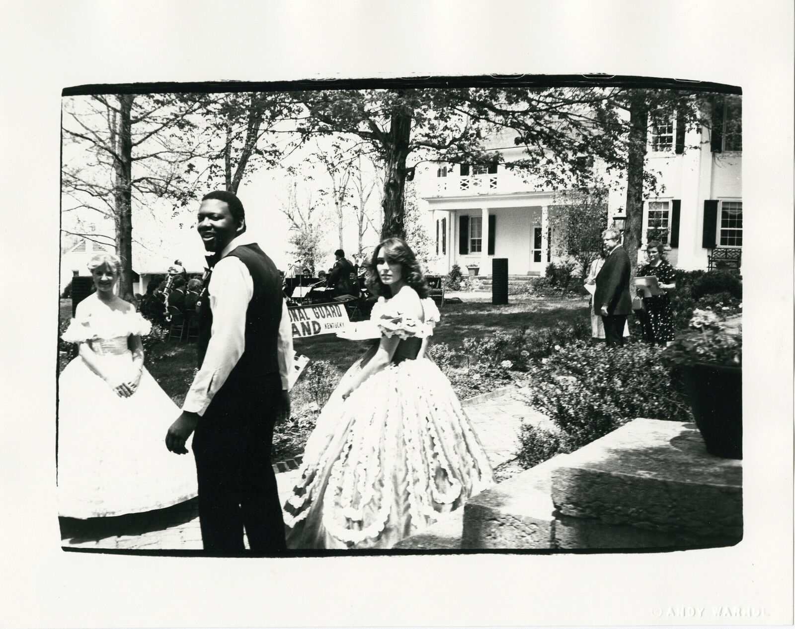 A black and white photo of a man and a woman walking in front of a house.