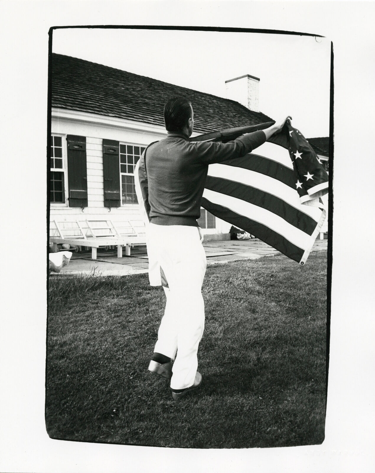 A man holding an American flag in front of a house.