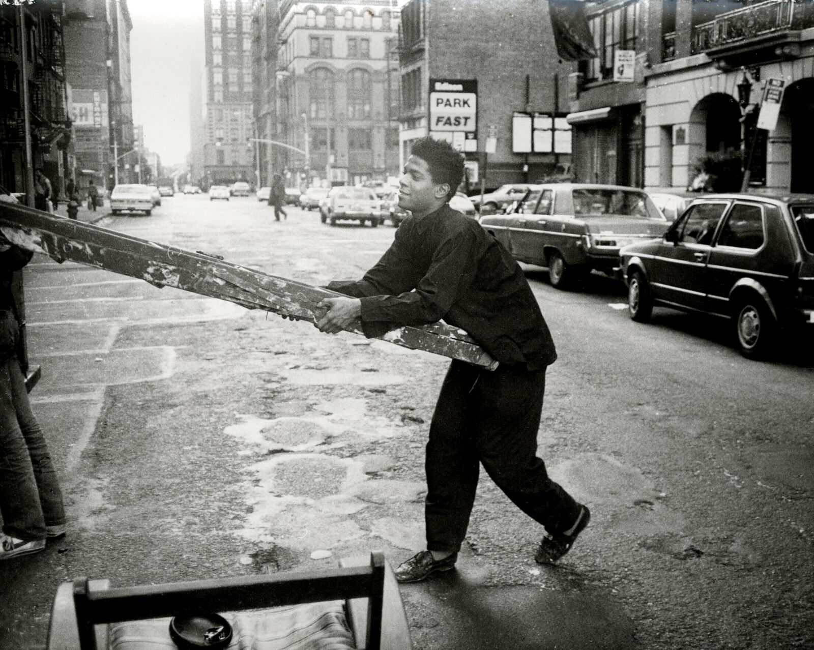 A man walking down a city street carrying a large piece of wood.