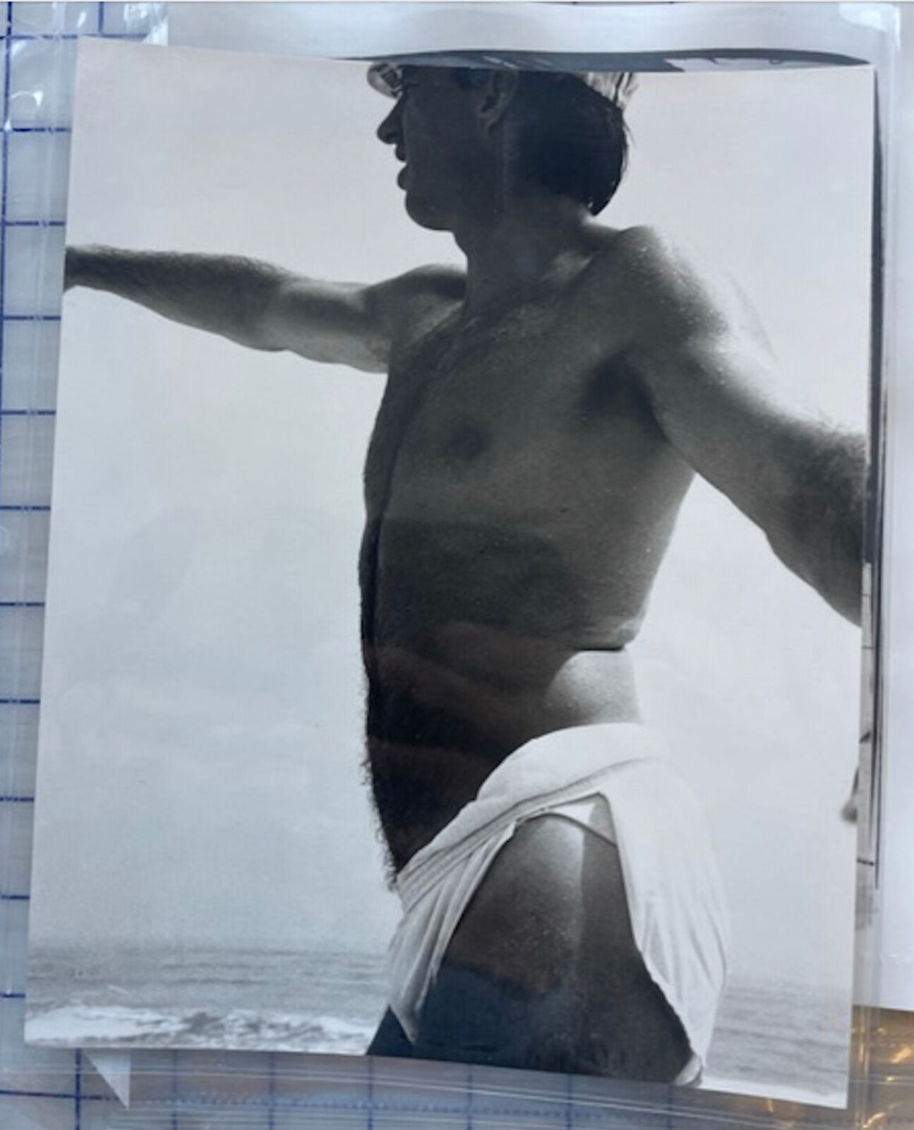 A shirtless man standing on a beach with his arms outstretched.