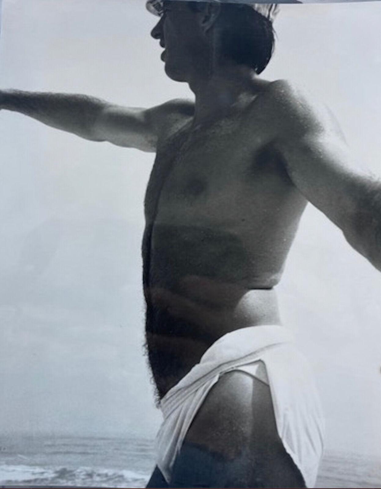 A shirtless man standing on a beach with his arms outstretched.