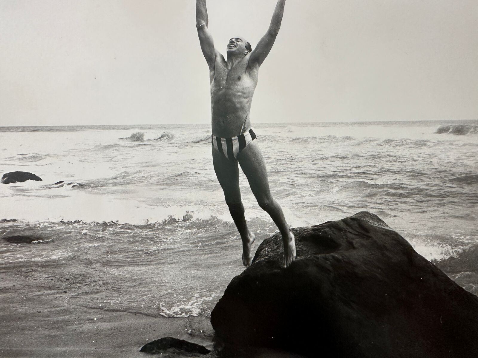 A man standing on top of a rock in the ocean.