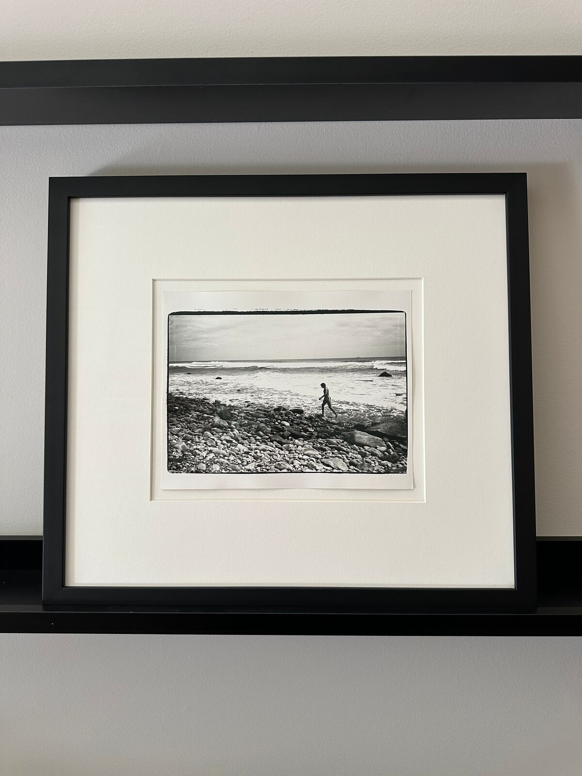 A black and white photo of a person walking on a rocky beach.