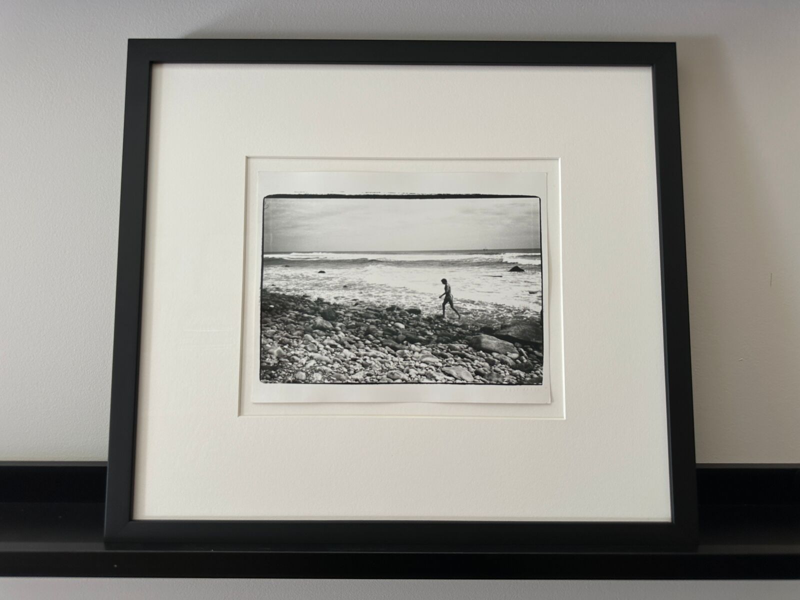 A black and white photo of a person walking on a rocky beach.