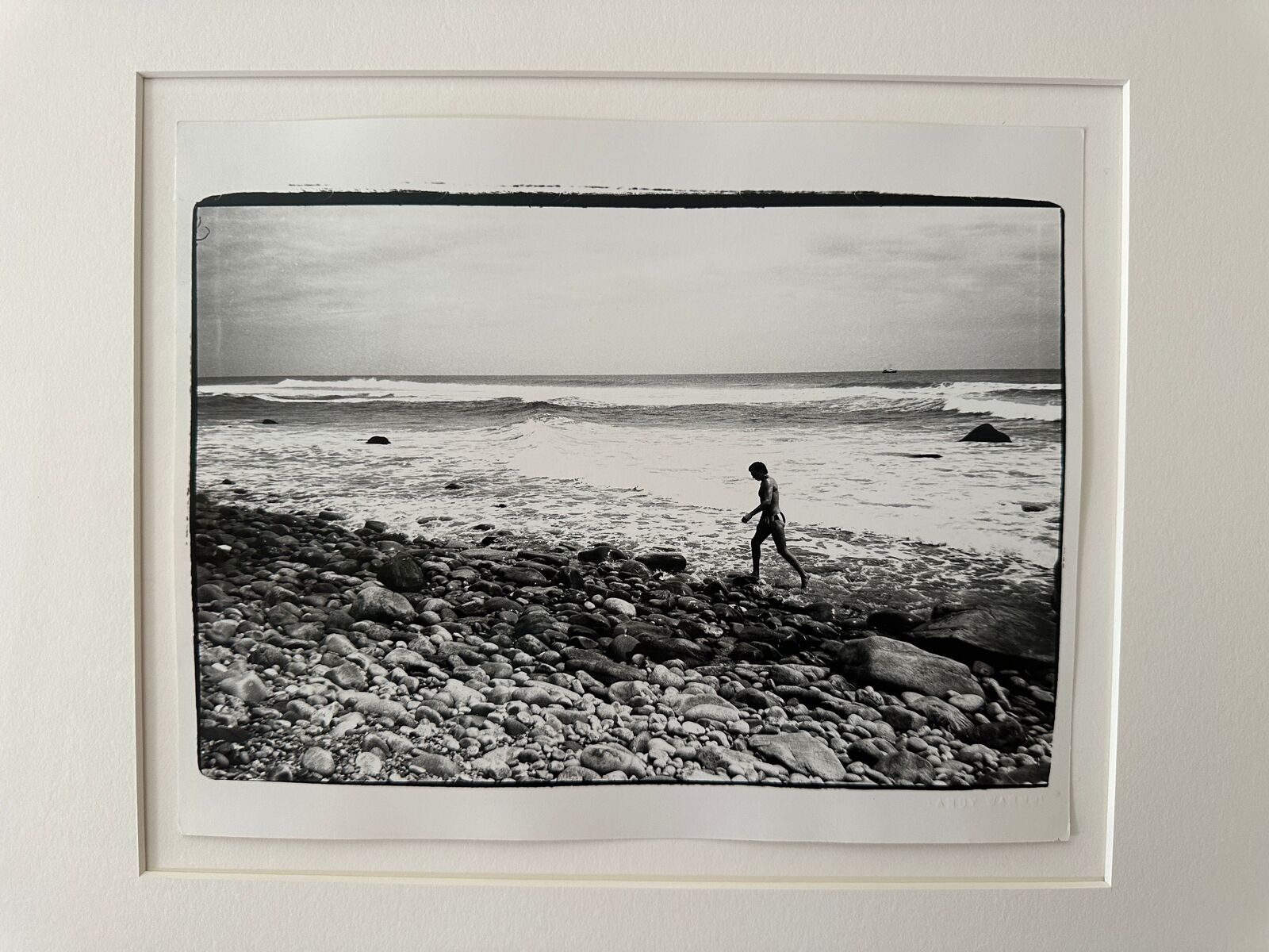 A black and white photo of a person walking on a rocky beach.