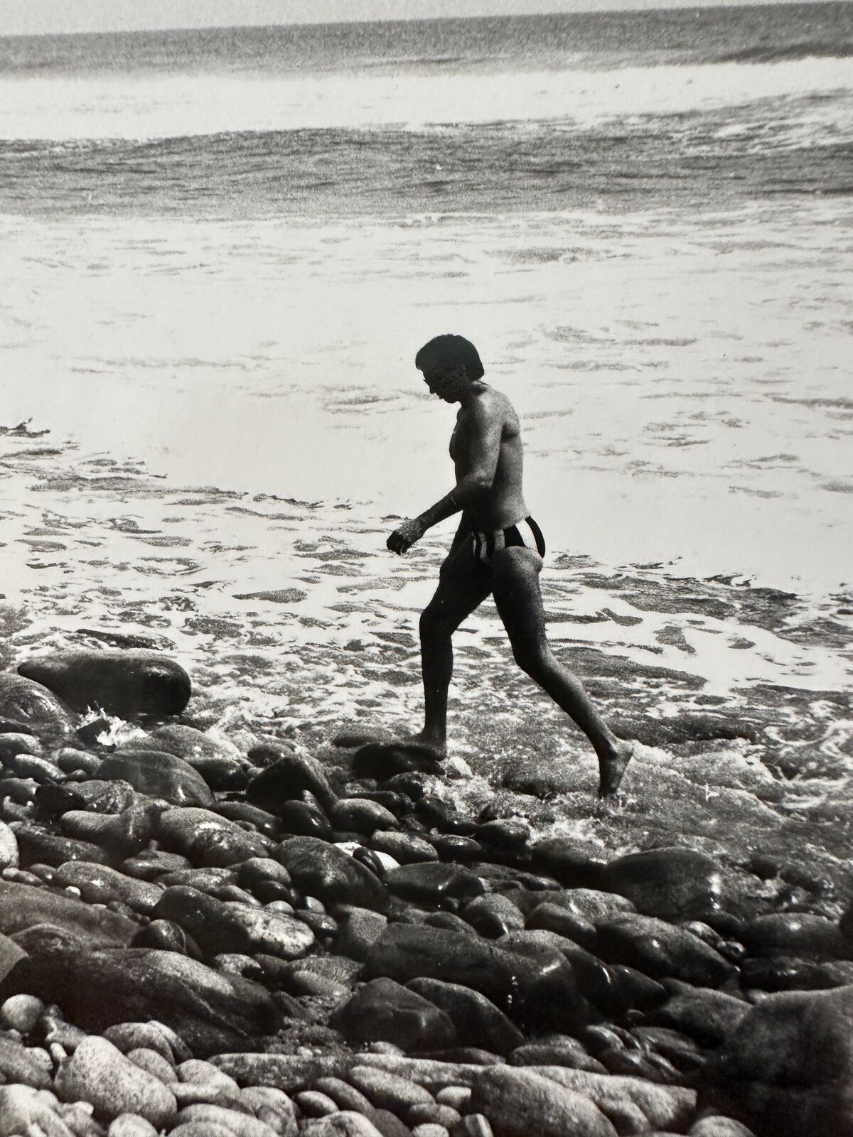 A black and white photo of a person walking on a rocky beach.
