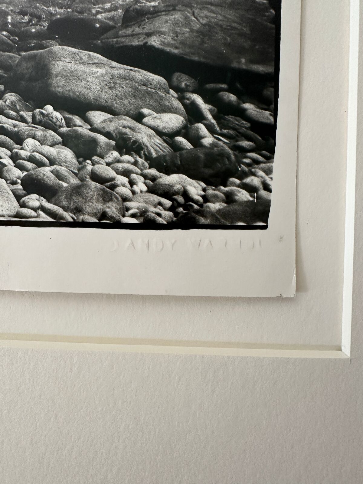 A black and white photo of a person walking on a rocky beach.