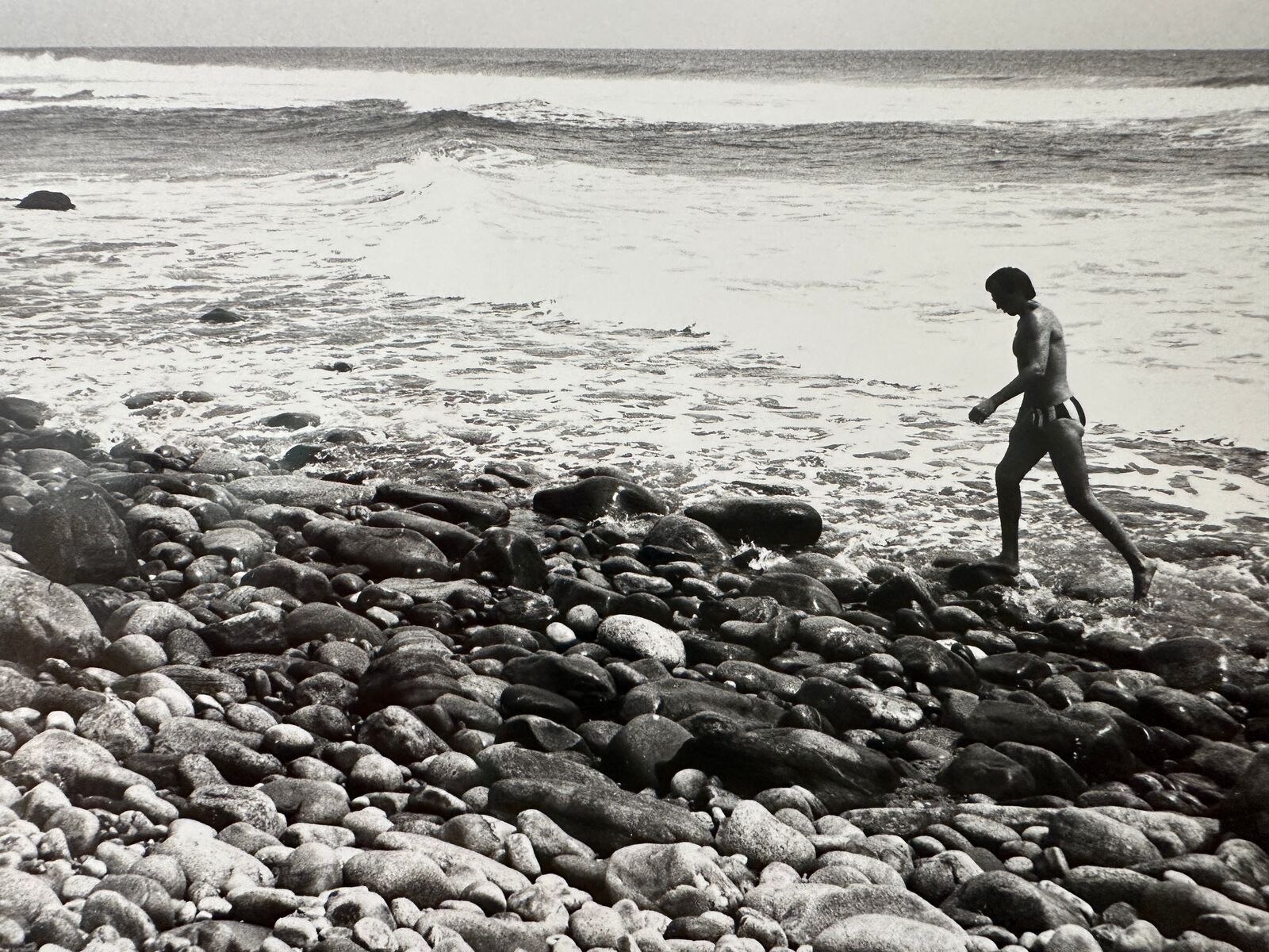 A black and white photo of a person walking on a rocky beach.