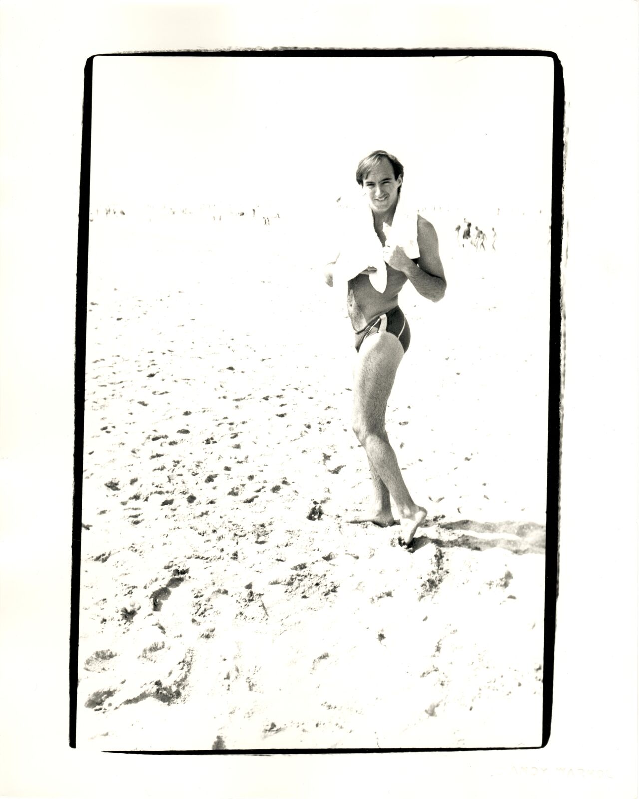 A black and white photo of a man in a bathing suit on the beach.